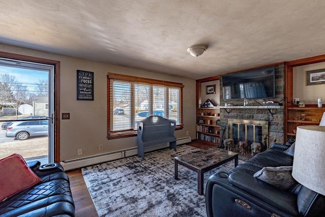 living area featuring baseboard heating, a stone fireplace, wood finished floors, and a textured ceiling