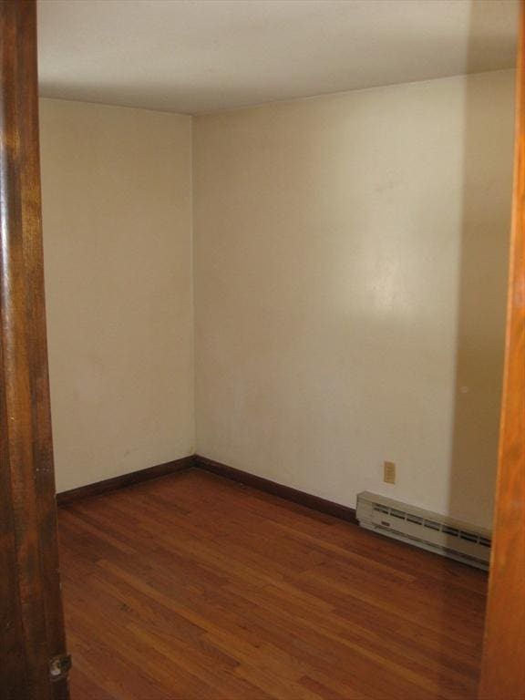 spare room with baseboards, baseboard heating, and wood finished floors