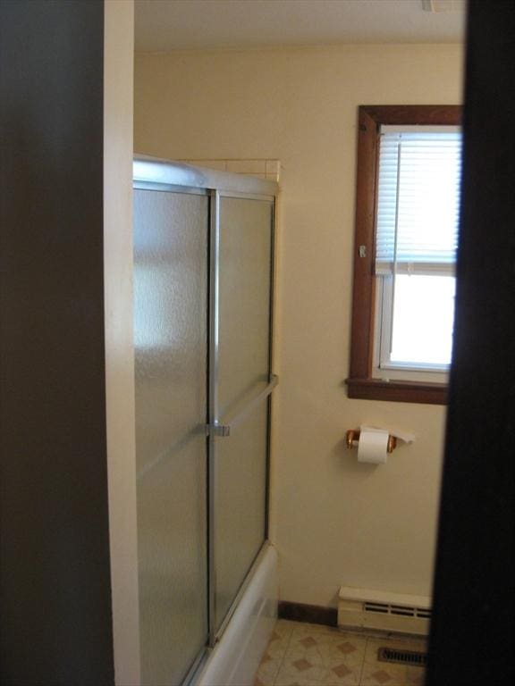 bathroom featuring bath / shower combo with glass door, baseboard heating, tile patterned floors, and baseboards