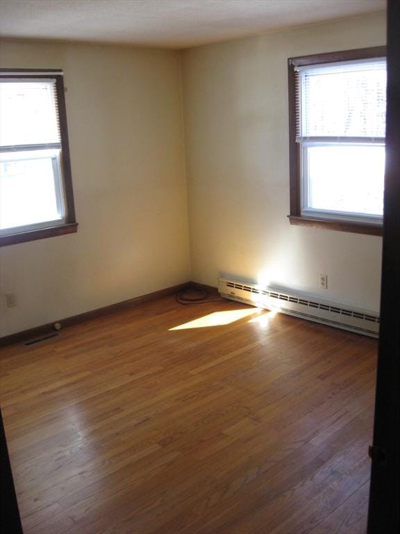 empty room with a baseboard radiator, baseboards, and wood finished floors