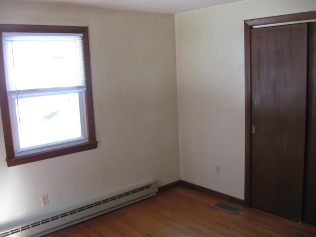 unfurnished room featuring a baseboard heating unit, visible vents, baseboards, and wood finished floors