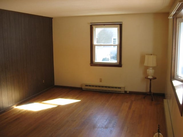 unfurnished room with baseboard heating, wood finished floors, and baseboards