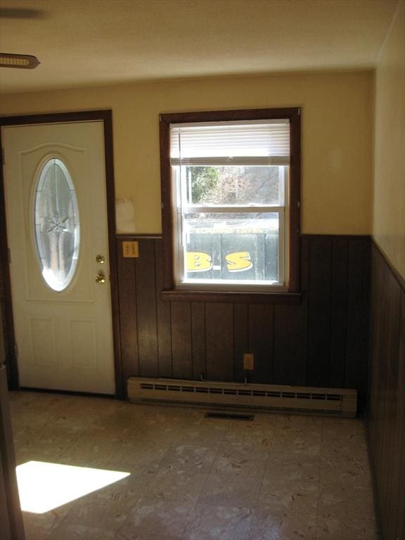 foyer entrance with a baseboard radiator, wooden walls, and wainscoting