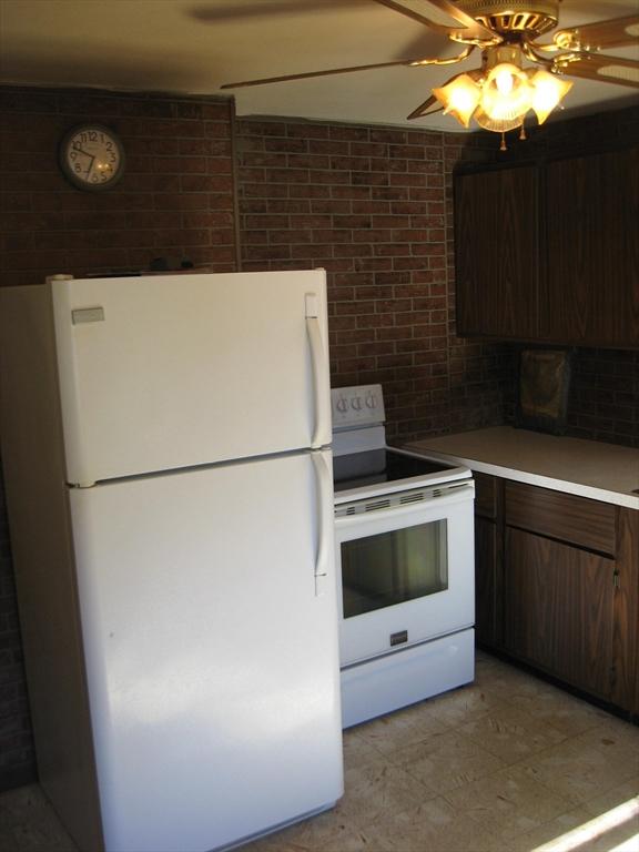 kitchen featuring dark brown cabinetry, white appliances, a ceiling fan, brick wall, and light countertops