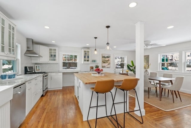 kitchen with stainless steel appliances, white cabinetry, a center island, and wall chimney range hood