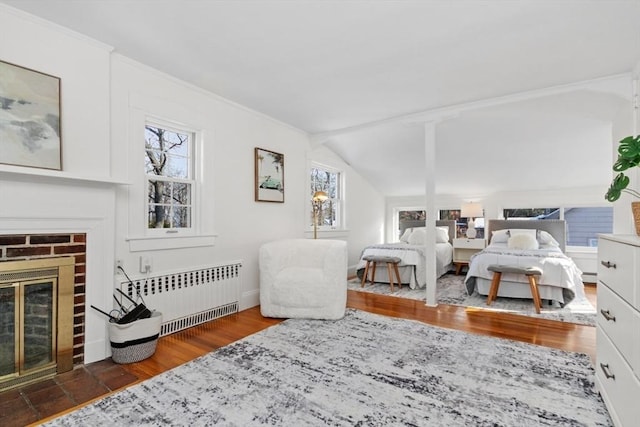 bedroom featuring radiator, dark wood-type flooring, a fireplace, ornamental molding, and vaulted ceiling