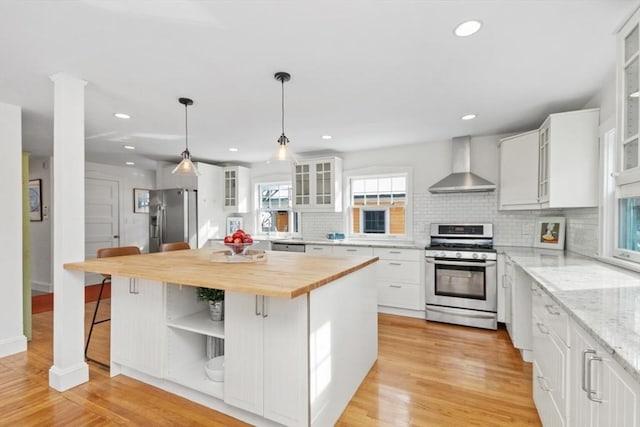 kitchen with white cabinetry, stainless steel appliances, wall chimney exhaust hood, and a kitchen island