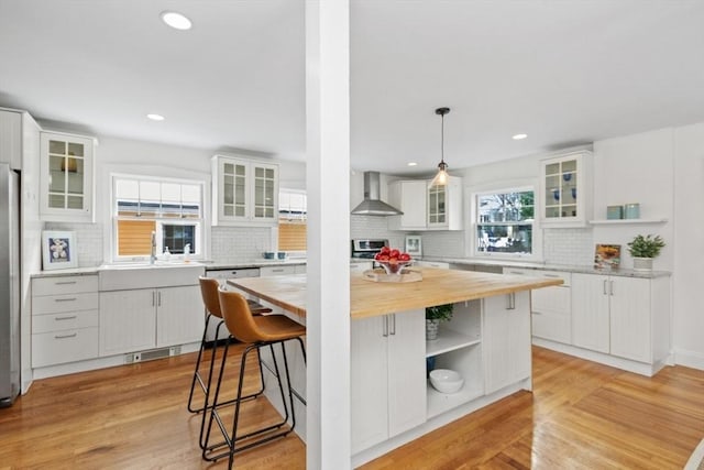 kitchen featuring white cabinetry, wall chimney range hood, pendant lighting, and a center island