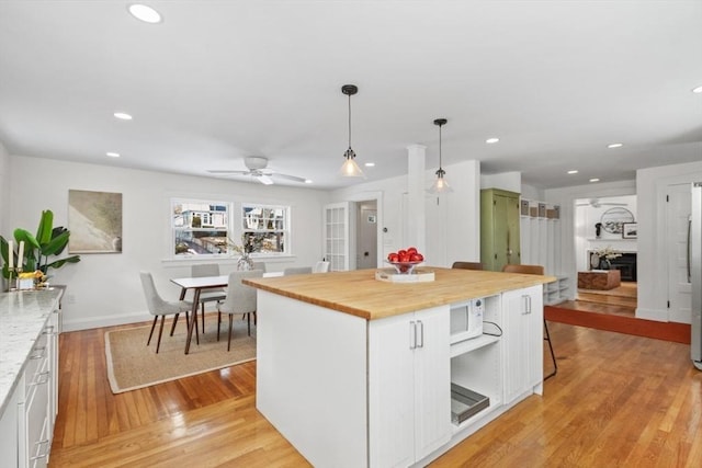 kitchen with pendant lighting, wood counters, white cabinets, a center island, and light hardwood / wood-style floors