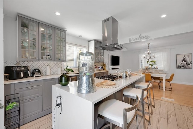 45 Olney Ave, Springfield, MA 01119 - kitchen featuring gray cabinetry, island exhaust hood, stainless steel gas cooktop, glass insert cabinets, and backsplash
