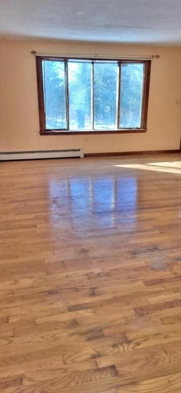 empty room with a healthy amount of sunlight, light hardwood / wood-style flooring, and a baseboard heating unit