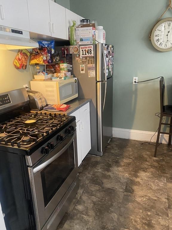 kitchen featuring baseboards, white cabinets, dark countertops, stainless steel appliances, and under cabinet range hood