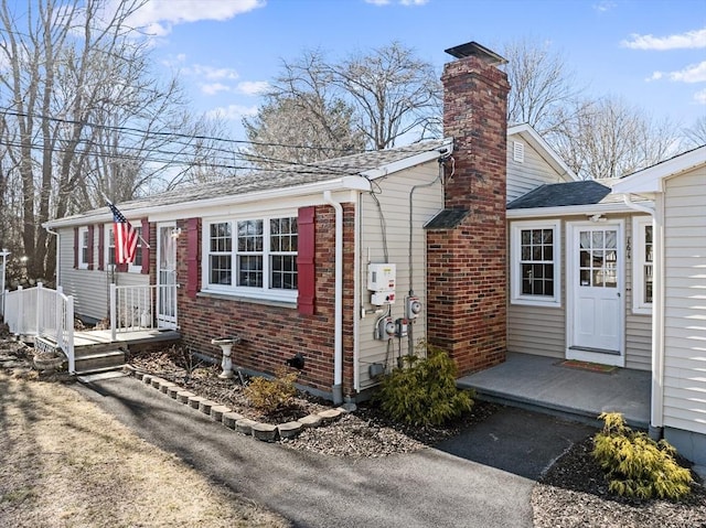 view of front of home with brick siding, a chimney, and a shingled roof