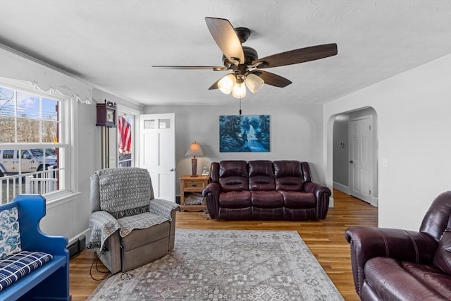 living room with a ceiling fan, visible vents, wood finished floors, and arched walkways