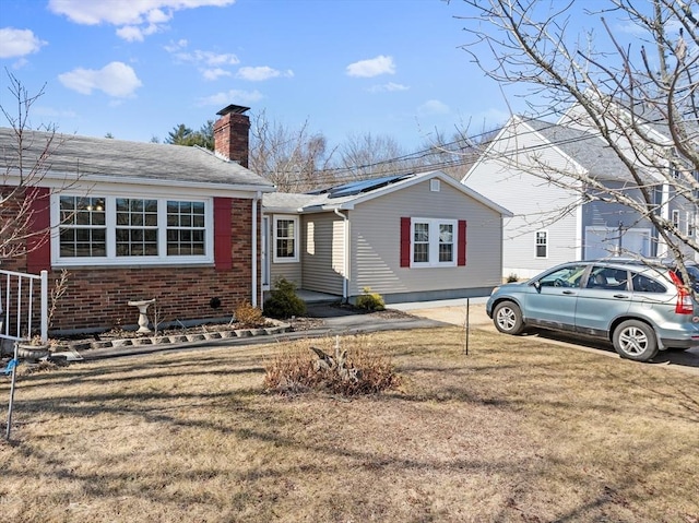 view of front of home with brick siding, solar panels, a chimney, and a front lawn