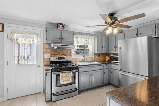 kitchen with a sink, gray cabinetry, stainless steel appliances, under cabinet range hood, and dark countertops