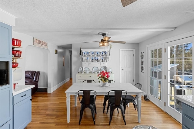 dining space with light wood-style flooring, a ceiling fan, baseboards, and a textured ceiling