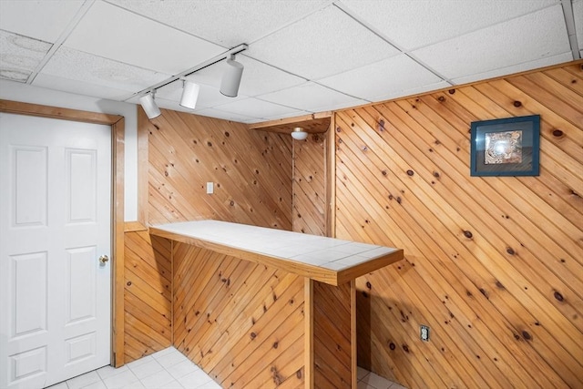 bar with tile counters, rail lighting, wooden walls, and a paneled ceiling