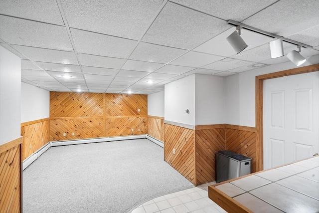 basement with track lighting, a drop ceiling, light carpet, and wood walls