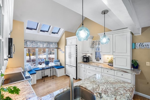 kitchen with lofted ceiling with skylight, decorative light fixtures, white cabinetry, sink, and paneled fridge