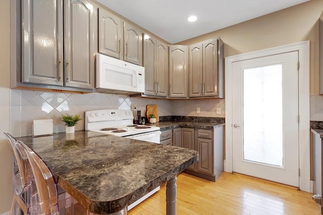 34 Warren St Unit 3, Stoneham, MA 02180 - kitchen featuring white appliances, a peninsula, light wood-style floors, a kitchen bar, and decorative backsplash
