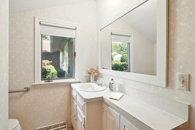 half bathroom with vanity, visible vents, toilet, and wallpapered walls