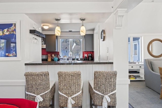 kitchen featuring a sink, exhaust hood, decorative backsplash, dark countertops, and decorative light fixtures