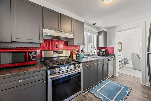 kitchen with dark countertops, gray cabinetry, appliances with stainless steel finishes, a sink, and under cabinet range hood