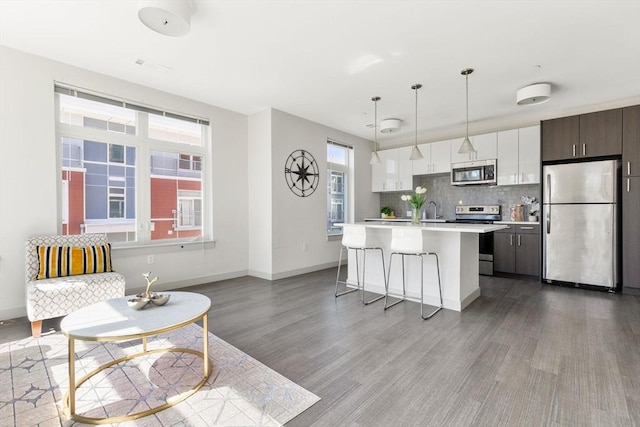 kitchen with white cabinets, hanging light fixtures, an island with sink, appliances with stainless steel finishes, and dark brown cabinets