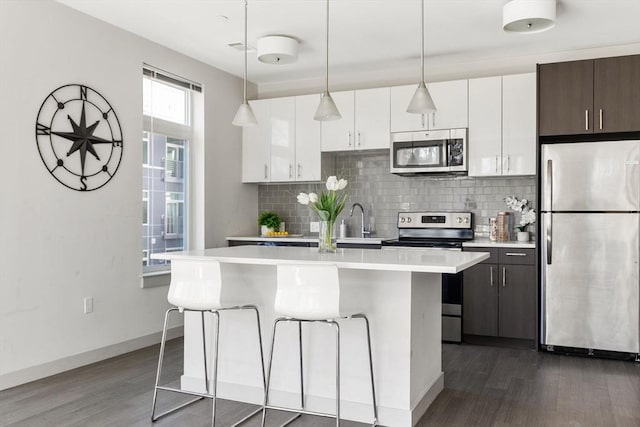 kitchen featuring stainless steel appliances, a kitchen breakfast bar, tasteful backsplash, dark brown cabinets, and a center island with sink