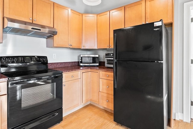 kitchen with black appliances, dark stone counters, light brown cabinets, and light hardwood / wood-style flooring