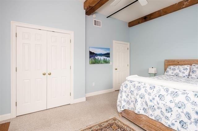 bedroom with ceiling fan, a closet, light carpet, and beamed ceiling