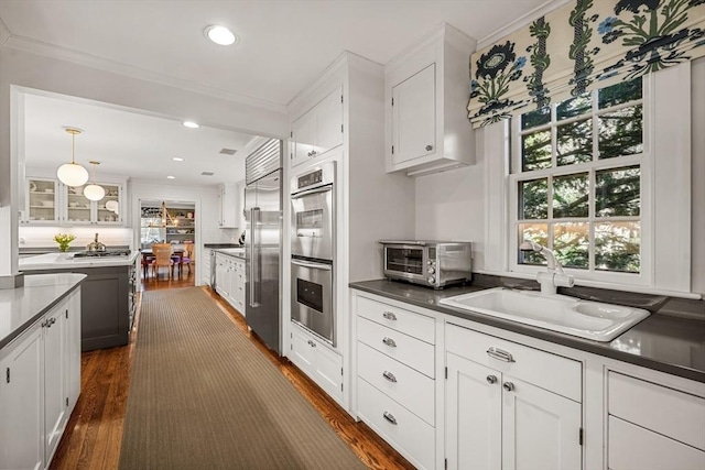 kitchen featuring a toaster, a sink, ornamental molding, stainless steel appliances, and white cabinetry