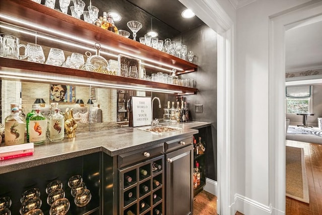 bar with indoor wet bar, a sink, wood finished floors, and ornamental molding