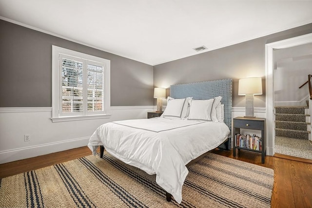 bedroom featuring visible vents, a wainscoted wall, wood finished floors, and crown molding