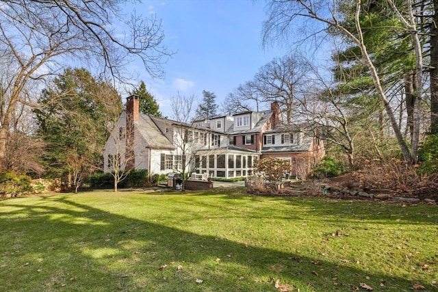 back of house featuring a yard, a sunroom, and a chimney