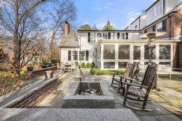 back of property featuring a chimney, an outdoor fire pit, a patio, and a sunroom