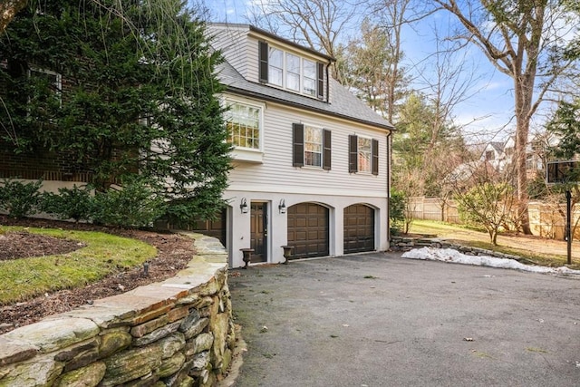 view of home's exterior featuring fence, an attached garage, driveway, and a shingled roof