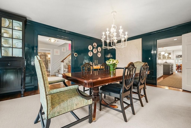 dining room featuring stairs, a chandelier, crown molding, and a decorative wall