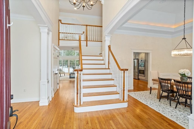 entrance foyer with wood finished floors, a notable chandelier, decorative columns, and stairs