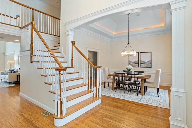 stairs featuring a tray ceiling, wood finished floors, decorative columns, and crown molding