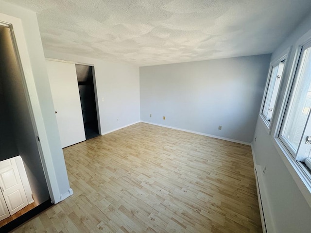 empty room featuring baseboards, a textured ceiling, and light wood-style flooring