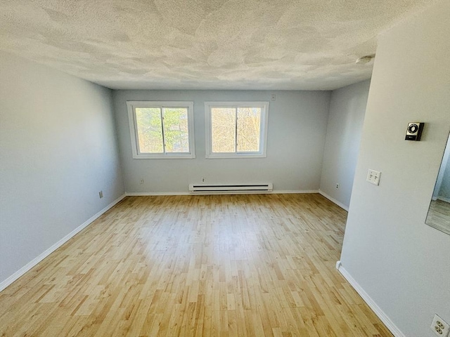 spare room featuring a baseboard heating unit, wood finished floors, baseboards, and a textured ceiling