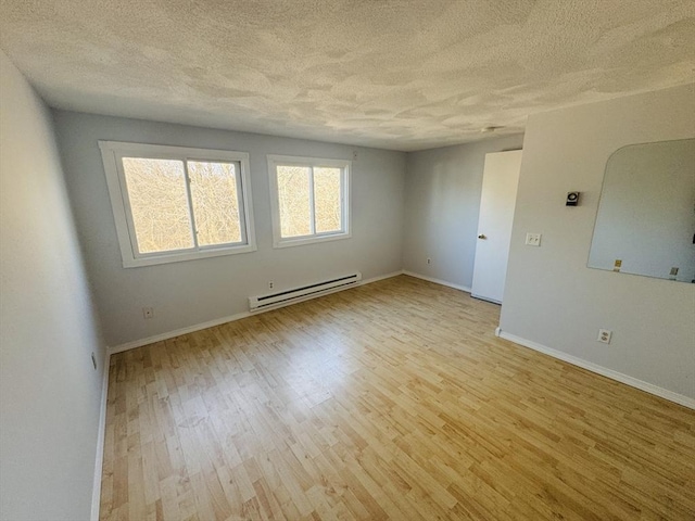 spare room featuring light wood-style floors, baseboards, baseboard heating, and a textured ceiling