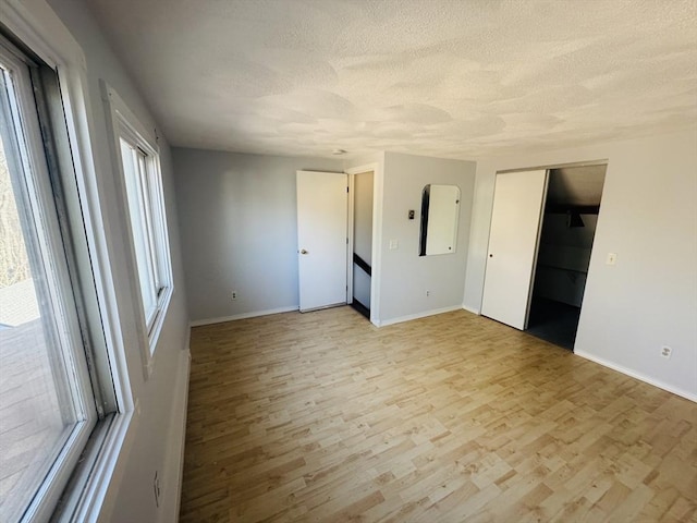 spare room with light wood-style floors, baseboards, and a textured ceiling