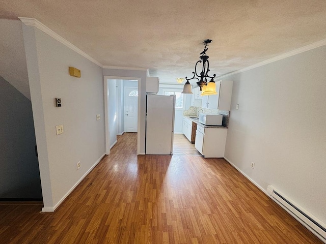 unfurnished dining area with wood finished floors, crown molding, a baseboard radiator, baseboards, and a chandelier