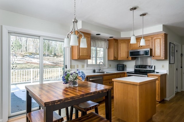 kitchen with a center island, light countertops, appliances with stainless steel finishes, a sink, and wood finished floors