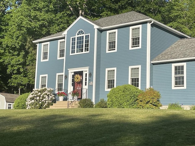 colonial inspired home featuring a front lawn and a shingled roof