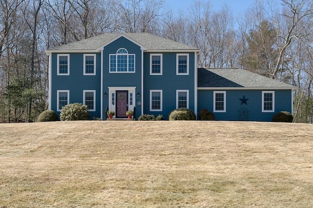 colonial-style house featuring roof with shingles and a front yard