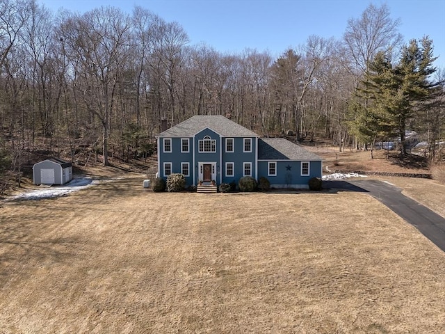 colonial home with a storage unit, a front lawn, and an outbuilding